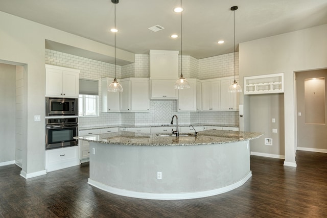 kitchen featuring white cabinetry, appliances with stainless steel finishes, light stone countertops, and an island with sink