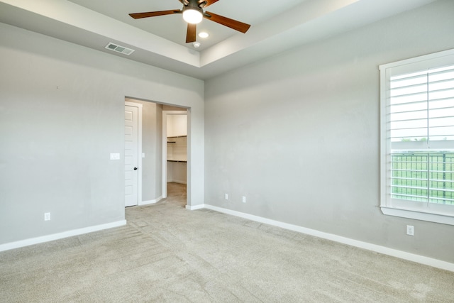 empty room with plenty of natural light, light carpet, ceiling fan, and a tray ceiling