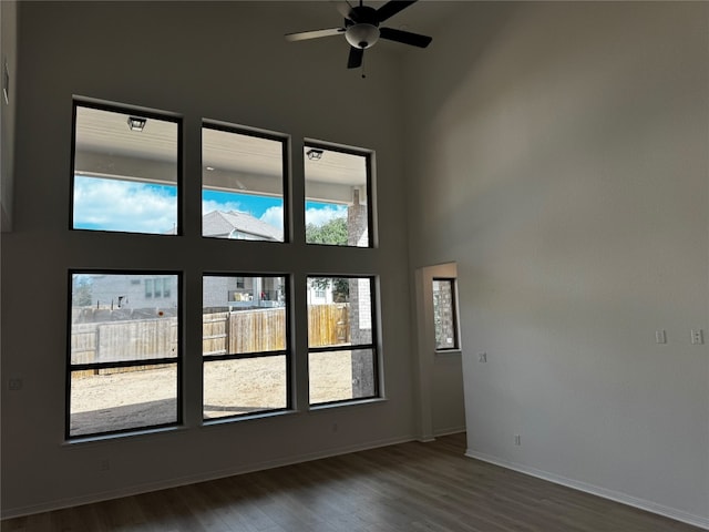 unfurnished room featuring a towering ceiling, dark hardwood / wood-style floors, and ceiling fan