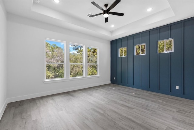 empty room with a tray ceiling, light wood-type flooring, and ceiling fan