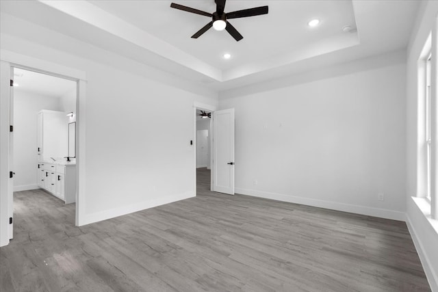 spare room featuring light wood-type flooring, ceiling fan, and a raised ceiling