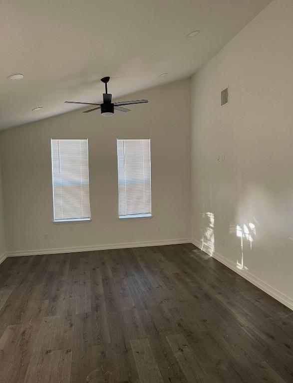 empty room with dark wood-style flooring, visible vents, a ceiling fan, vaulted ceiling, and baseboards