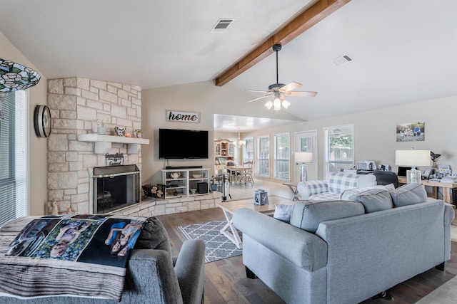 living room with vaulted ceiling with beams, hardwood / wood-style flooring, a stone fireplace, and ceiling fan