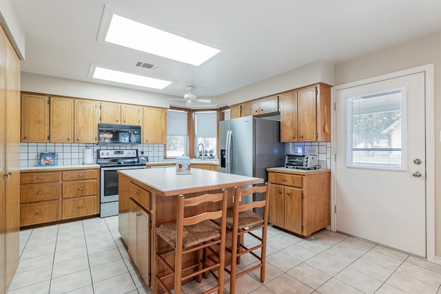 kitchen featuring a skylight, stainless steel appliances, a center island, a kitchen bar, and decorative backsplash