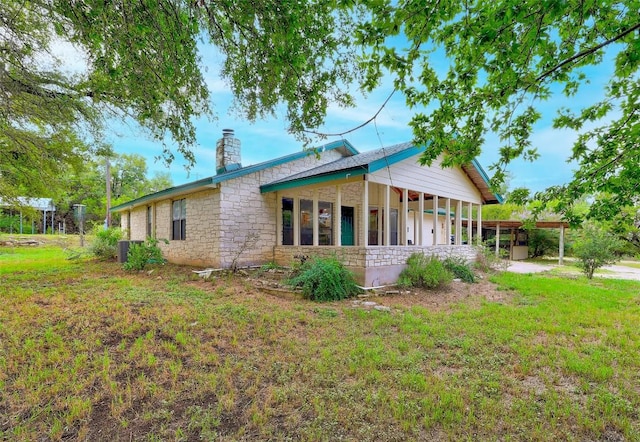 back of property featuring stone siding, a lawn, and a chimney