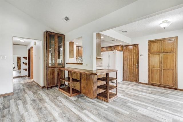 kitchen featuring a textured ceiling, vaulted ceiling, white refrigerator, and light wood-type flooring