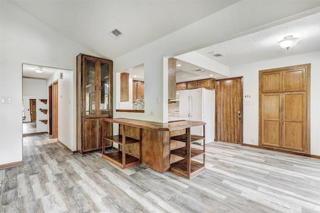 kitchen featuring brown cabinetry, freestanding refrigerator, vaulted ceiling, a textured ceiling, and light wood-type flooring