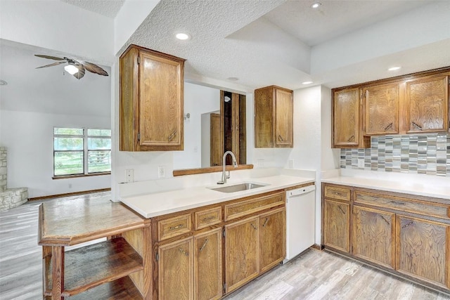 kitchen with brown cabinetry, light wood-type flooring, white dishwasher, and a sink