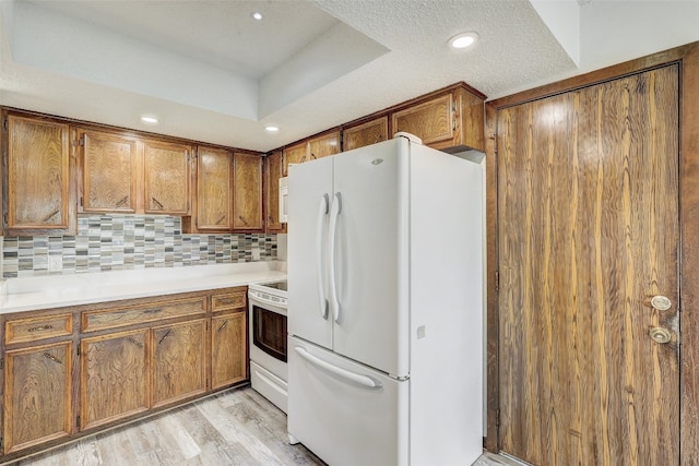 kitchen featuring light hardwood / wood-style flooring, white appliances, decorative backsplash, a textured ceiling, and a tray ceiling