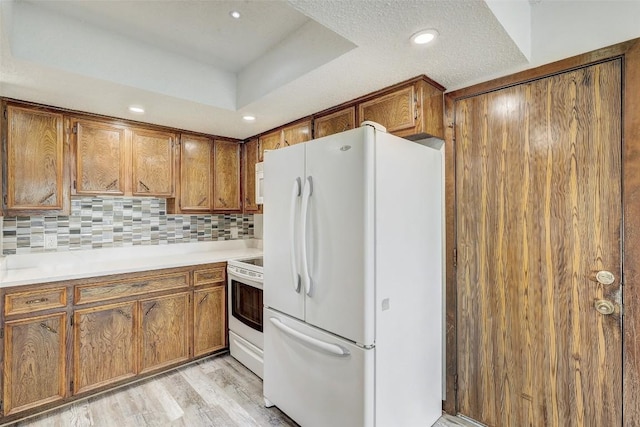 kitchen featuring brown cabinets, white appliances, a raised ceiling, and decorative backsplash