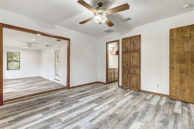 empty room with baseboards, light wood-style flooring, visible vents, and a textured ceiling