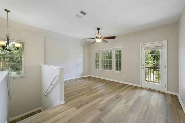 spare room with light wood-type flooring and ceiling fan with notable chandelier