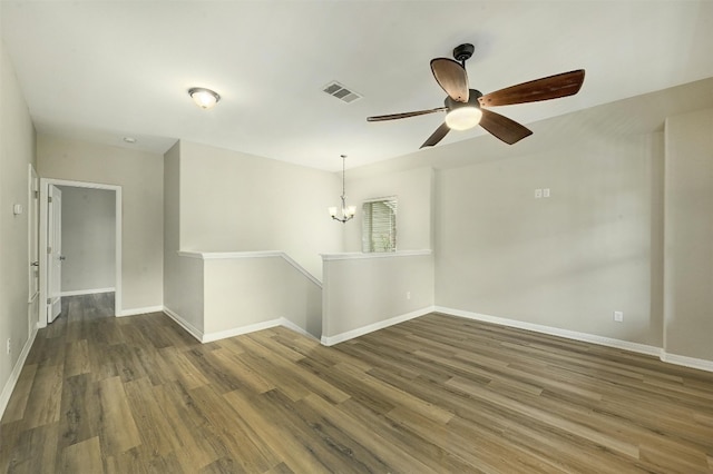 empty room with ceiling fan with notable chandelier and dark wood-type flooring