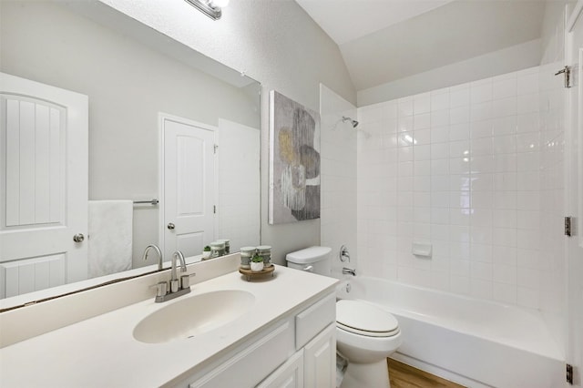 full bathroom with toilet, tiled shower / bath, wood-type flooring, vaulted ceiling, and vanity