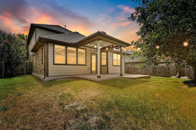 back house at dusk featuring a lawn and a patio area