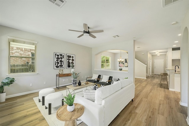 living room with ceiling fan with notable chandelier, sink, and light hardwood / wood-style flooring