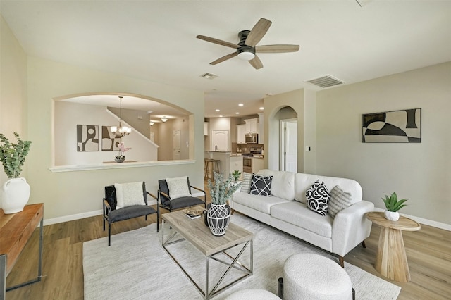 living room with ceiling fan with notable chandelier and light hardwood / wood-style flooring