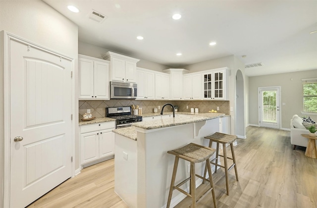 kitchen with light stone countertops, stainless steel appliances, light wood-type flooring, and white cabinetry