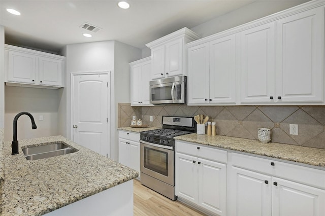 kitchen featuring light stone counters, light hardwood / wood-style floors, sink, white cabinetry, and appliances with stainless steel finishes