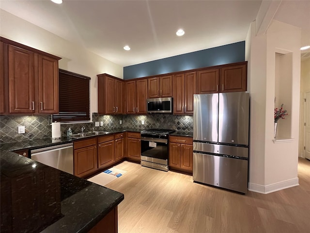 kitchen featuring sink, backsplash, dark stone counters, stainless steel appliances, and light wood-type flooring