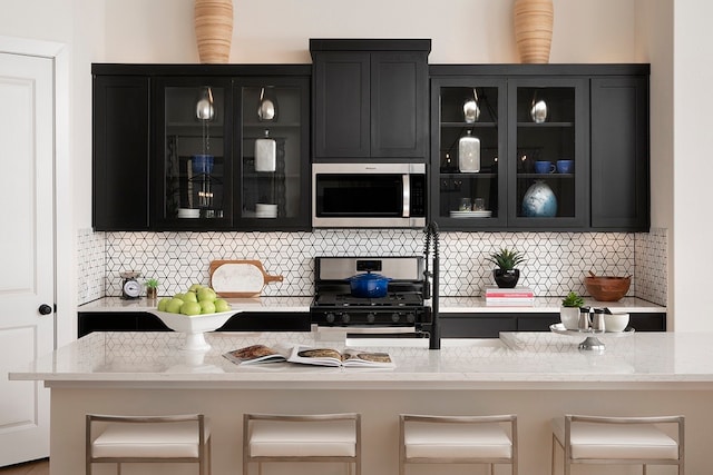 bar featuring stainless steel appliances, light stone countertops, and tasteful backsplash