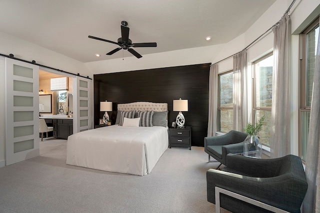 bedroom featuring ceiling fan, light carpet, ensuite bathroom, and a barn door