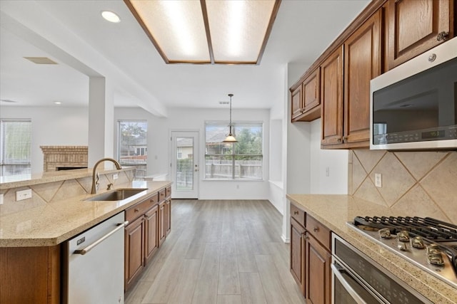 kitchen with appliances with stainless steel finishes, sink, light stone counters, and light hardwood / wood-style flooring