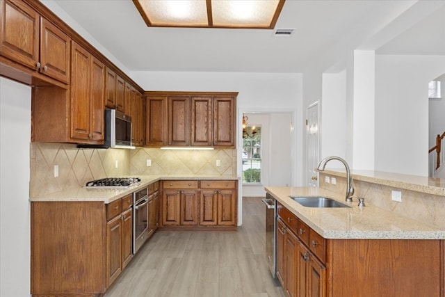 kitchen with sink, appliances with stainless steel finishes, light stone countertops, backsplash, and light hardwood / wood-style flooring