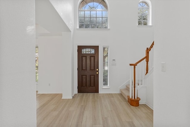 entryway with a towering ceiling, a healthy amount of sunlight, and light hardwood / wood-style flooring