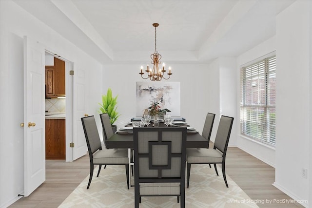 dining area with a tray ceiling, an inviting chandelier, and light hardwood / wood-style floors