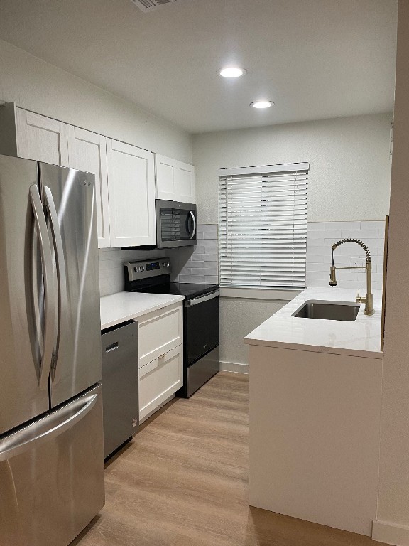 kitchen with sink, white cabinets, light hardwood / wood-style floors, and stainless steel appliances