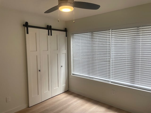 unfurnished bedroom with light hardwood / wood-style floors, a barn door, and ceiling fan