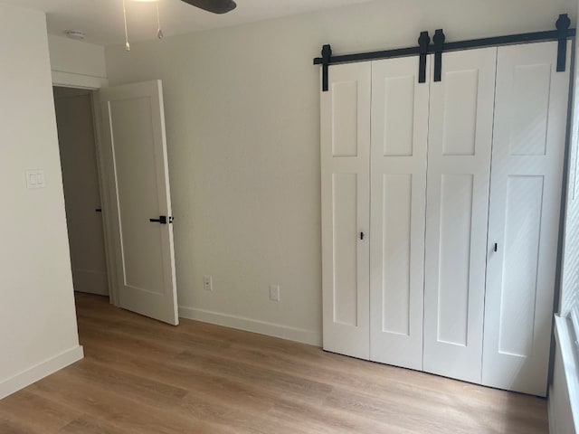 unfurnished bedroom with light hardwood / wood-style floors, a barn door, and ceiling fan