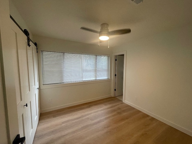 unfurnished bedroom featuring ceiling fan, light wood-type flooring, and a barn door