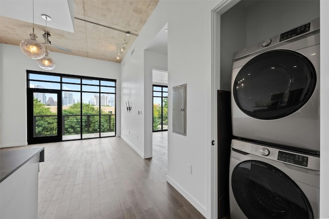 washroom with stacked washer / dryer, electric panel, hardwood / wood-style flooring, and track lighting