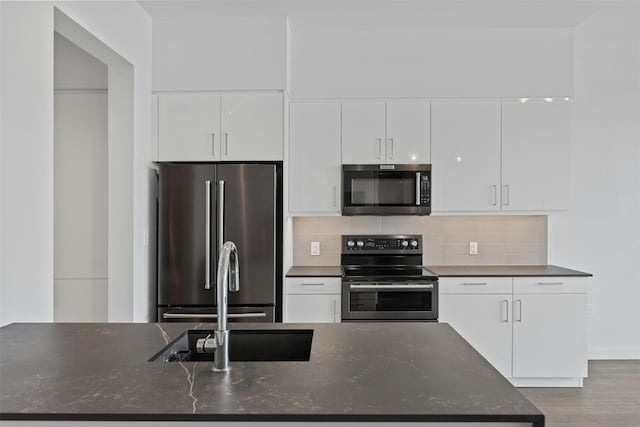 kitchen featuring appliances with stainless steel finishes, white cabinets, backsplash, light wood-type flooring, and dark stone countertops