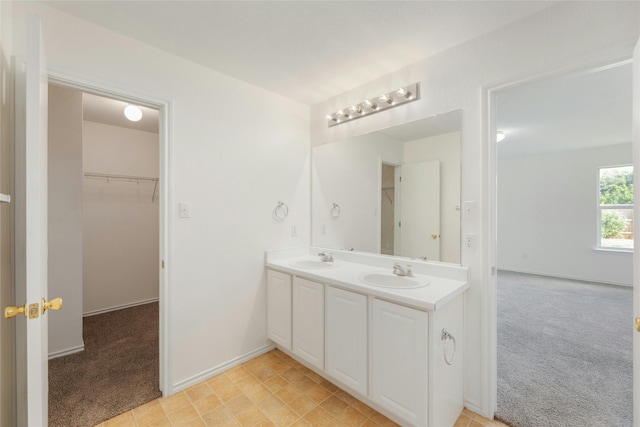 bathroom with a walk in closet, a sink, baseboards, and double vanity