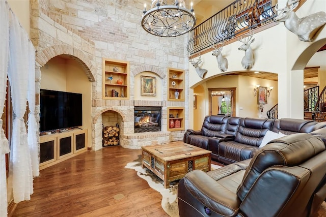 living room featuring hardwood / wood-style floors, built in features, a fireplace, a chandelier, and a high ceiling