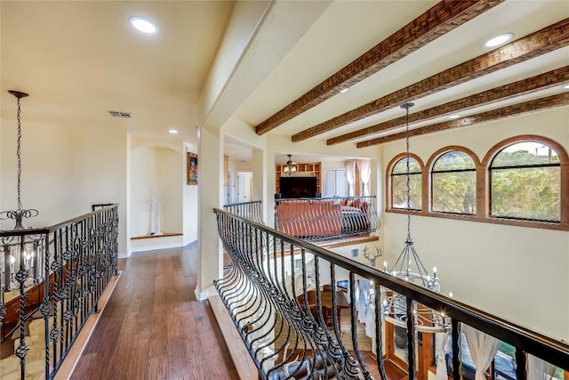 corridor featuring beam ceiling, hardwood / wood-style flooring, and a chandelier