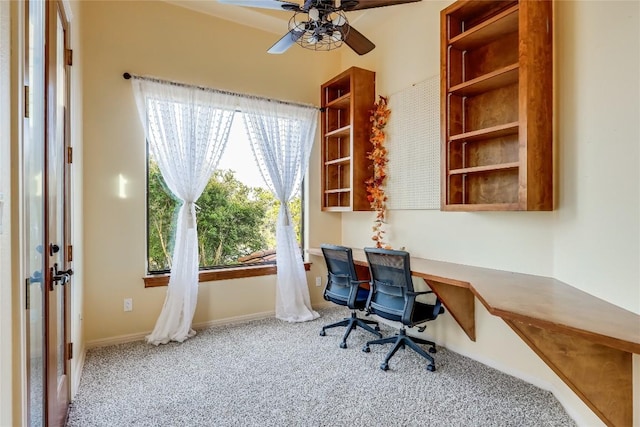 carpeted home office with built in desk and ceiling fan