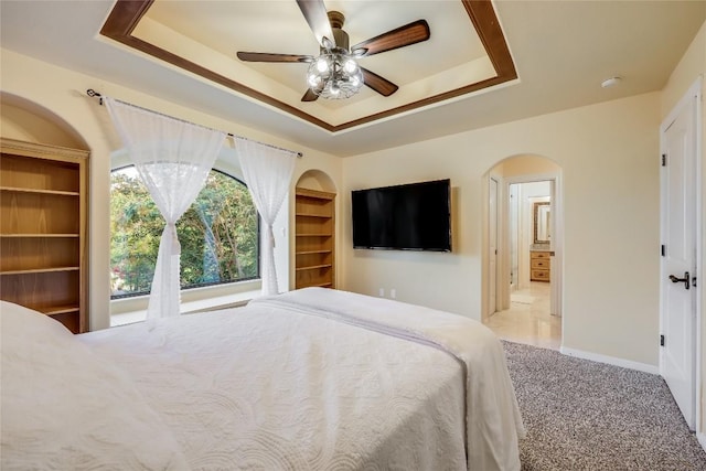 bedroom featuring ensuite bath, ceiling fan, and a tray ceiling