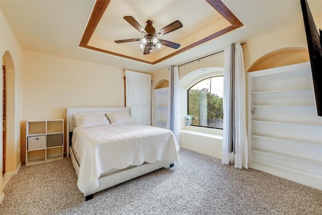 carpeted bedroom featuring a raised ceiling and ceiling fan