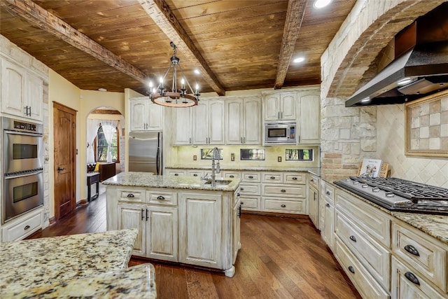 kitchen with sink, hanging light fixtures, built in appliances, light stone countertops, and a center island with sink