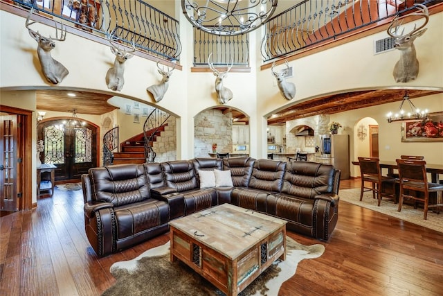 living room with a towering ceiling, dark hardwood / wood-style floors, a chandelier, and french doors