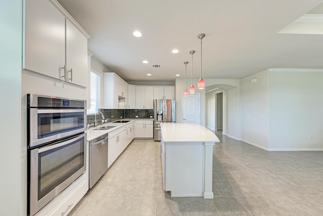 kitchen featuring white cabinets, hanging light fixtures, ornamental molding, a center island, and stainless steel appliances