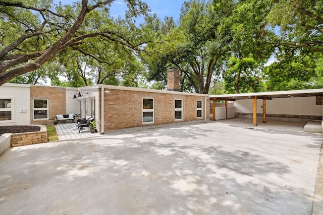 view of front facade featuring concrete driveway, a chimney, a patio area, a carport, and brick siding