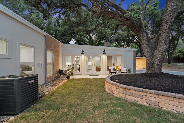 back of property featuring brick siding, a chimney, stucco siding, a lawn, and central AC unit