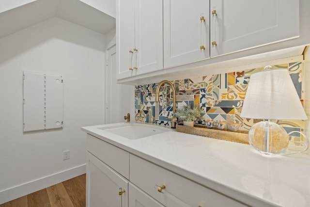 kitchen featuring baseboards, white cabinets, wood finished floors, light countertops, and a sink