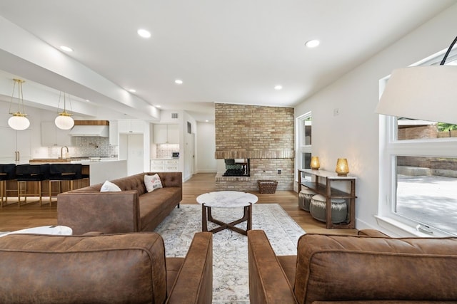 living room with a brick fireplace, a wealth of natural light, and wood finished floors