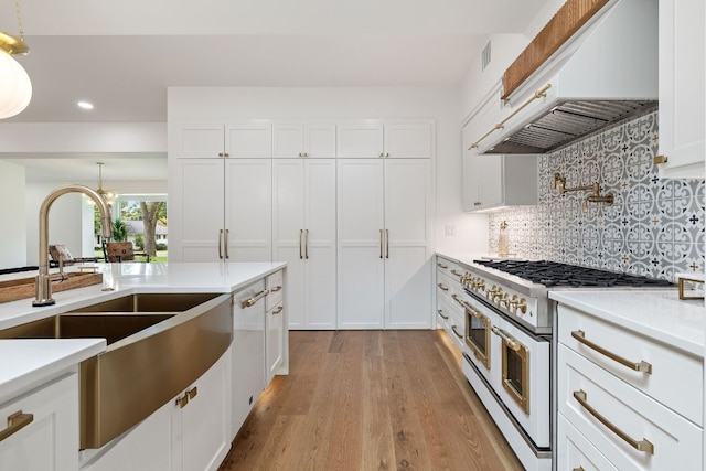 kitchen with range with two ovens, custom range hood, a sink, and white cabinetry